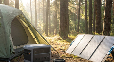 A portable power station and foldable solar panel set up beside a tent at a forest campsite