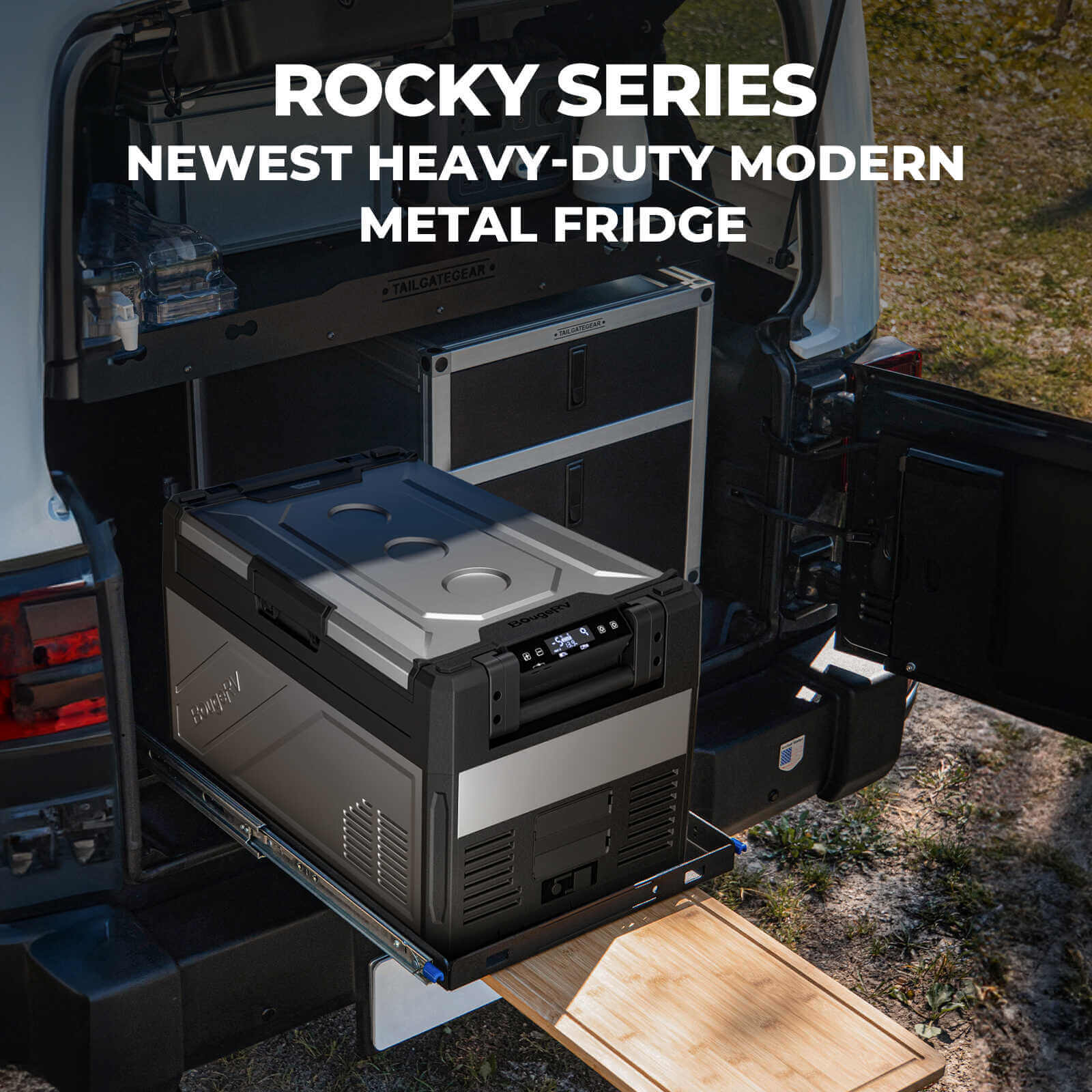 A BougeRV Rocky Series 69QT Heavy-Duty Modern Dual Zone metal fridge is securely installed on a sliding platform in the back of a vehicle, surrounded by other camping equipment. The text above proudly declares, "ROCKY SERIES NEWEST HEAVY-DUTY MODERN DUAL ZONE FRIDGE.