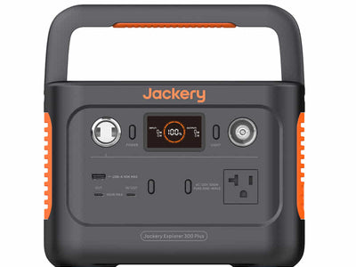 The Jackery portable power station is black with orange accents and features a handle, digital display, USB-A/USB-C ports, AC/DC outputs, and a car charger socket.