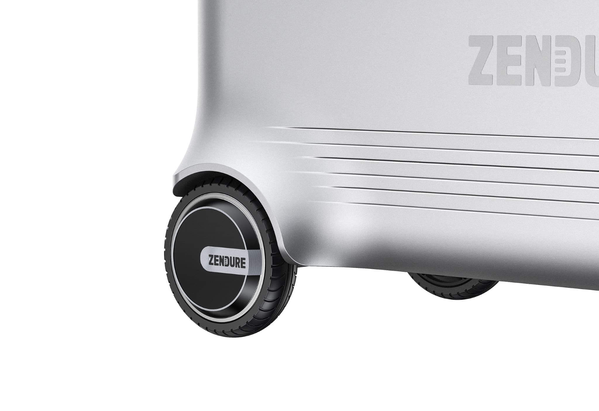 Close-up of the bottom corner of a Zendure suitcase showing two black wheels with "Zendure" on the hubcaps. The silver design, ideal for travelers, has a smooth finish with sleek horizontal grooves.