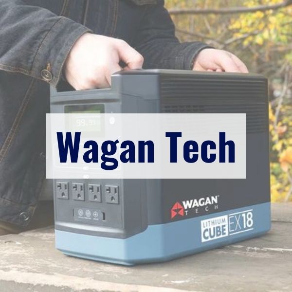 A person holding a Wagan Tech Lithium Cube EX18 portable power station with three AC outlets, an LCD screen, and branded text on a blue overlay in the foreground. The device is placed on a wooden surface.