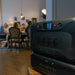 Two Bluetti power stations are stacked in the foreground, drawing the viewer’s attention. In the background, a group of people gathered around a dining table enjoy a warmly lit room. The focus remains on the Bluetti power stations.