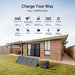 A Bluetti solar panel and portable power station are set up on the grass outside a modern brick house. Text above details input methods and charging times for the power station. The sky is clear and the yard is fenced.