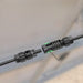 A close-up of two black Nature's Generator MC4 extension cables joined by a cylindrical connector, with an arrow showing assembly direction. The background is blurred.