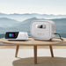 A Bluetti portable power station and a CPAP machine are placed on a round wooden table, with a scenic mountain landscape visible in the background through a large window.