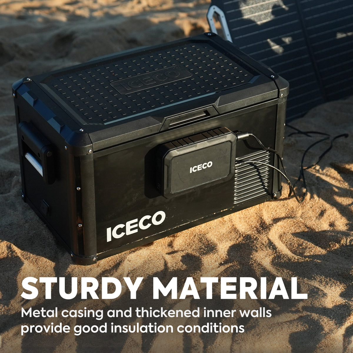 A black ICECO Wholesale cooler rests on the sand. This durable portable fridge freezer features a robust metal casing and reinforced inner walls. With its Secop compressor, it guarantees superior insulation and dependable cooling performance. The phrase "Sturdy Material" is prominently displayed at the bottom.