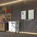 A home garage shows a Nature's Generator battery storage unit on the floor, connected by cable to a wall-mounted automatic transfer switch, with shelves, tools, and posters visible in the background.
