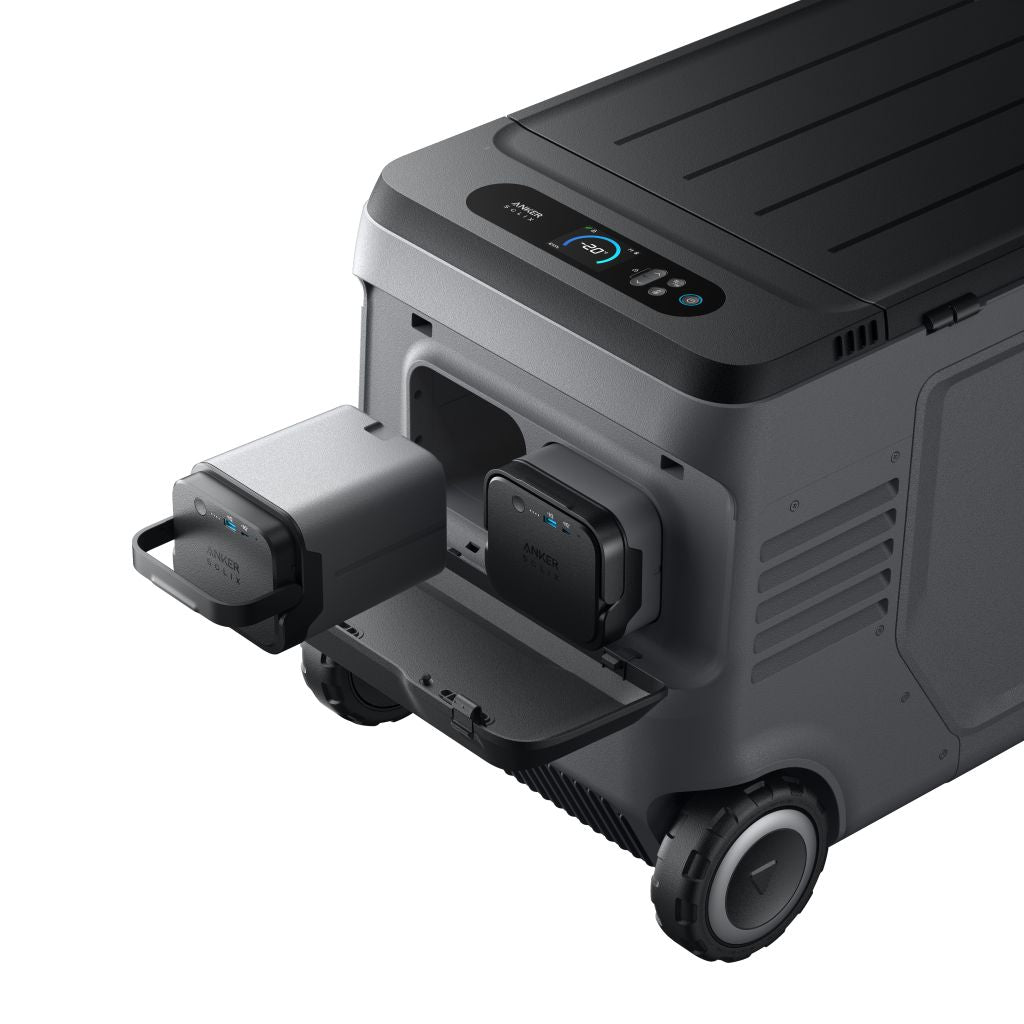 The Anker portable solar cooler is shown with wheels, a handle, a top control panel, and two removable battery modules, one partially pulled out from the front compartment.