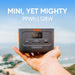 Someone holds a Jackery portable power station outdoors under a blue sky, with a blurry landscape in the background. The image text says "MINI, YET MIGHTY 99Wh | 128W.