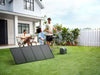 A family enjoys an outdoor meal on the lawn while an EcoFlow DELTA 3 1500 Portable Power Station with a reliable LiFePO4 battery provides backup power nearby. A house, table, and barbecue are visible in the background.