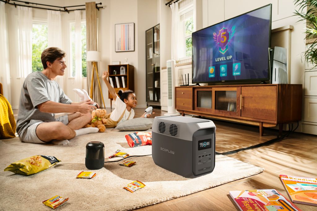 A man and child play video games on the living room floor, snacks around them, with an EcoFlow DELTA 3 1500 Portable Power Station (LiFePO4 battery) providing backup power in the foreground as "LEVEL UP" appears on the TV.