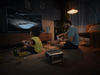 A child and an adult are playing video games in a dimly lit living room. The large TV displays a hockey game, with snacks and drinks nearby. An EcoFlow RIVER 3 Max portable power station ensures uninterrupted playtime with its X-Boost technology.