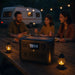 An EcoFlow RIVER 2 Pro Portable Power Station by EcoFlow sits on a picnic table near two lanterns as a family enjoys dinner outdoors, with a camper and string lights creating a warm, inviting atmosphere. No further product details are available.