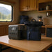 An EcoFlow portable power station and a dark blue backpack sit on a wooden table inside an RV kitchen.