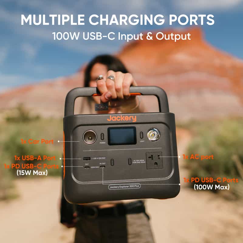 A person holds a Jackery portable power station, featuring USB-C (100W), USB-A, car port, and AC port, against a desert landscape. Labels highlight input/output capabilities.