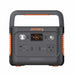 The Jackery portable power station is black with orange accents and features a handle, digital display, USB-A/USB-C ports, AC/DC outputs, and a car charger socket.