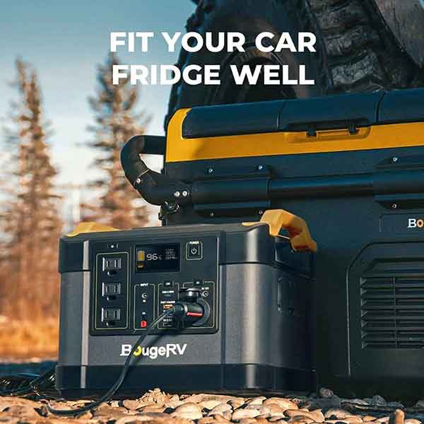 A BougeRV portable power station with an impressive 1200W output easily connects to the car refrigerator, showcasing a black and yellow design, in an outdoor setting. The phrase "Fit Your Car Fridge Well" appears above this arrangement, which is placed on a rocky surface with a partially visible vehicle tire in the background.