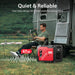 A man relaxes in a camping chair beside a trailer, reading next to a red PowerSmart 4800W quiet inverter generator. Its 67 dB operation delivers backup power for a peaceful outdoor environment.
