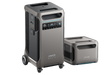 Two portable power stations are displayed. The larger model features wheels, a digital display panel with multiple ports, and is compatible with a solar panel. The smaller unit has a box-shaped design with visible vents. Both prominently showcase the brand name Anker, highlighting their reliability and innovation.