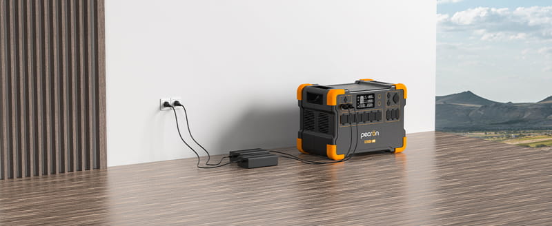 The Pecron E2000LFP, a portable power station accented in orange, is plugged into a wall socket in a modern room with wooden flooring. Equipped with a 2000W Pure Sine Wave Inverter, it is perfectly positioned near a corner that offers a scenic outdoor view through the window.