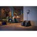 A person sits on a couch in a dimly lit living room where the EcoFlow DELTA Pro portable power station by EcoFlow is plugged into a wall outlet. The modern furniture and large potted plant in the room are optimally enhanced with efficient energy use, thanks to the X-Boost technology.
