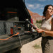 A woman in a desert landscape uses her tablet to manage the Jackery Solar Generator, acclaimed for its ultra-fast charging and smart app control, resting on a truck bed with mountains and clear skies in view.