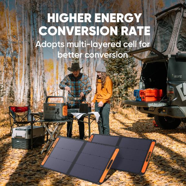 Two people set up a Jackery high efficiency solar panel near outdoor gear, a table, and a vehicle in an autumn forest. Overlay text: "Higher energy conversion rate. Multi-layered cell design boosts conversion.