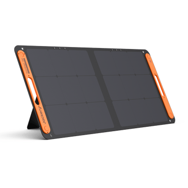 A Jackery foldable solar panel with a black surface and orange handles on both sides stands upright on its built-in kickstand against a plain white background.