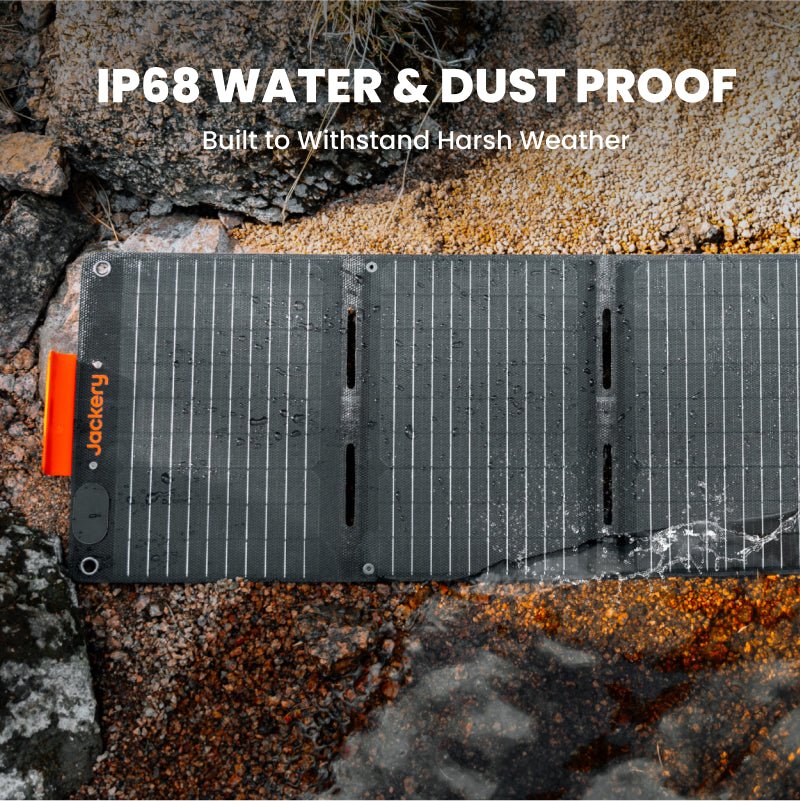 A Jackery portable solar panel, covered with water droplets and dust, sits outdoors on rocky ground. Text above reads, "IP68 WATER & DUST PROOF—Built to Withstand Harsh Weather." Ideal for powering your Jackery Explorer.