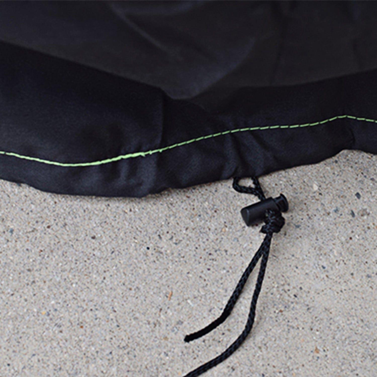 Close-up of a black 600D polyester fabric edge with green stitching from Nature's Generator, lying on concrete. A black drawstring with plastic toggle is threaded through the hem—ideal as a generator protective cover.