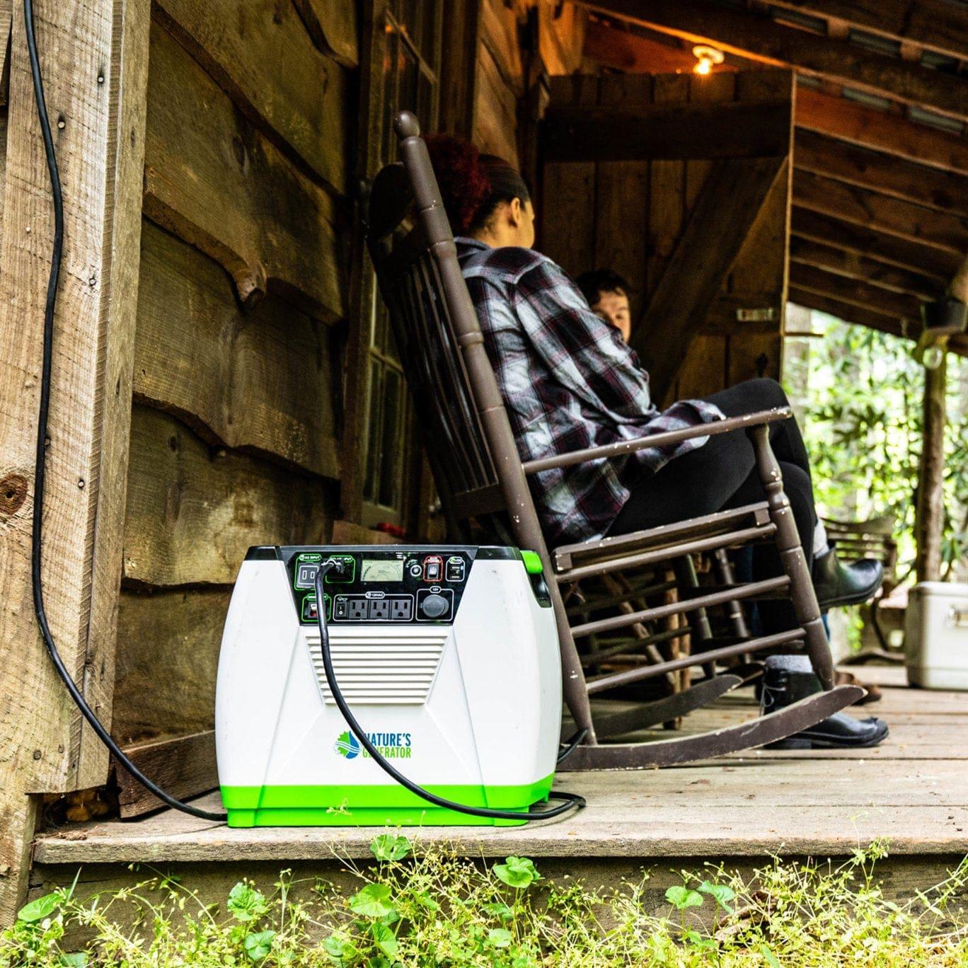 A Nature's Generator solar generator rests on a wooden porch by a cabin, while two people relax in rocking chairs, enjoying an off-grid retreat surrounded by greenery and rustic wooden walls.