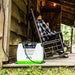 A Nature's Generator solar generator rests on a wooden porch by a cabin, while two people relax in rocking chairs, enjoying an off-grid retreat surrounded by greenery and rustic wooden walls.